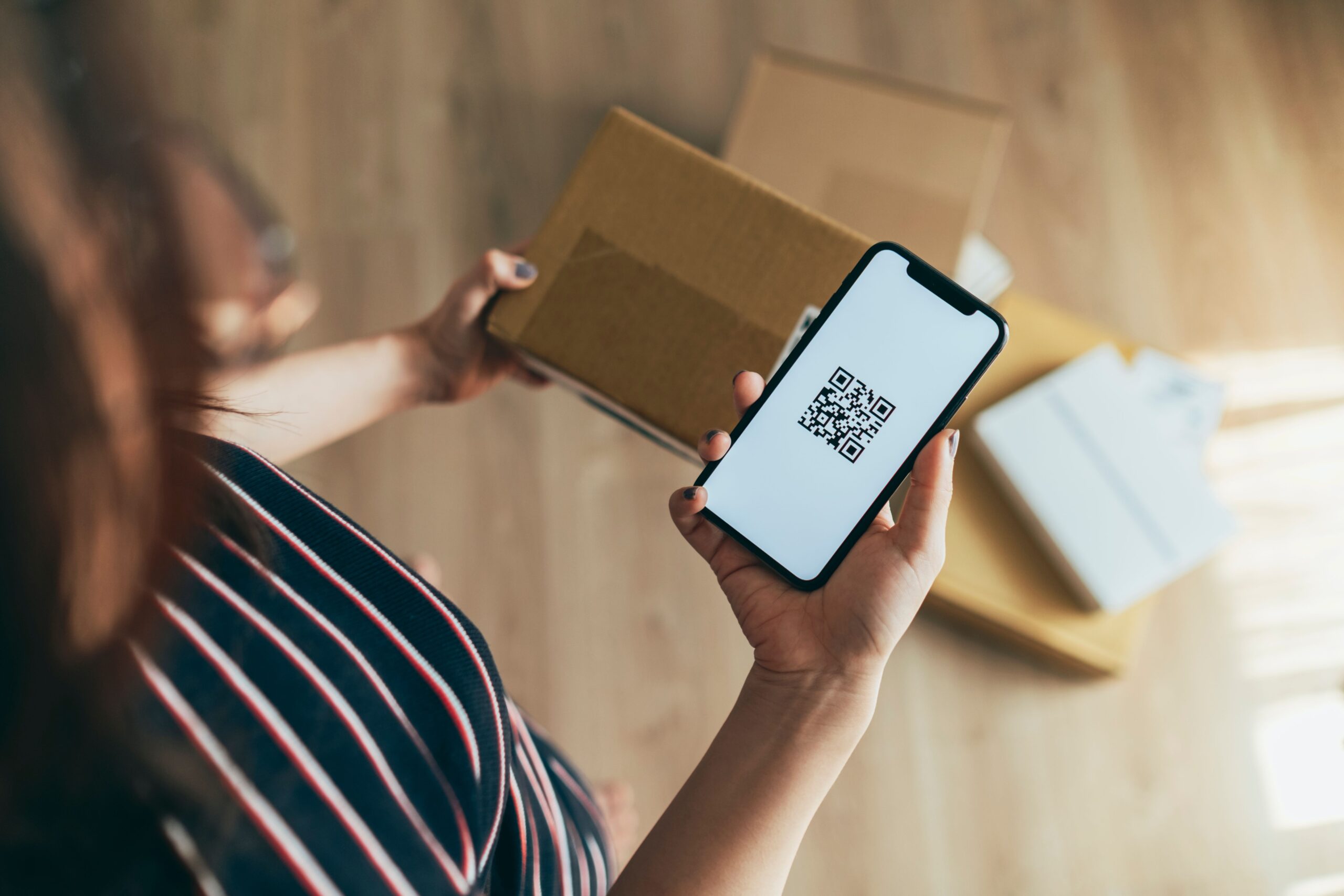 Photo to illustrate RMA, return merchandise authorization. Woman with a package and a QR code.